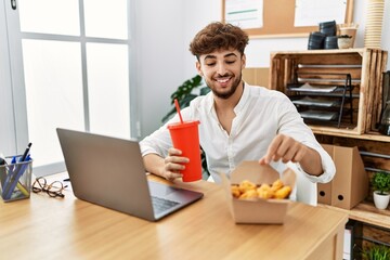 Wall Mural - Young arab man using laptop having lunch at office