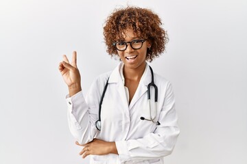 Canvas Print - Young african american woman wearing doctor uniform and stethoscope smiling with happy face winking at the camera doing victory sign. number two.