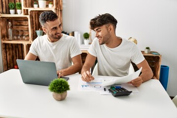 Two hispanic men couple smiling confident using laptop working at home