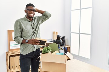 Poster - Young african american businessman unboxing box at the office smiling confident touching hair with hand up gesture, posing attractive and fashionable