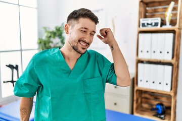 Wall Mural - Young physiotherapist man working at pain recovery clinic dancing happy and cheerful, smiling moving casual and confident listening to music