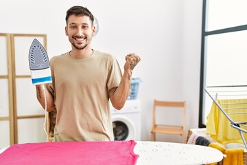 Sticker - Young handsome man ironing clothes at home screaming proud, celebrating victory and success very excited with raised arm