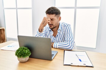 Canvas Print - Young handsome man with beard working at the office using computer laptop tired rubbing nose and eyes feeling fatigue and headache. stress and frustration concept.