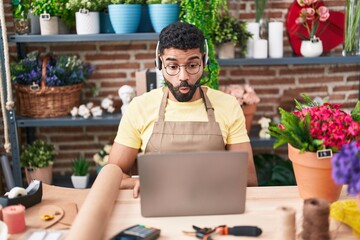 Wall Mural - Hispanic man with beard working at florist shop doing video call scared and amazed with open mouth for surprise, disbelief face