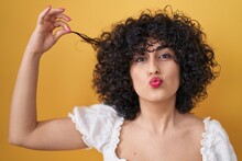 Young Brunette Woman With Curly Hair Holding Curl Looking At The Camera Blowing A Kiss Being Lovely And Sexy. Love Expression.