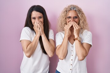 Canvas Print - Mother and daughter standing together over pink background laughing and embarrassed giggle covering mouth with hands, gossip and scandal concept