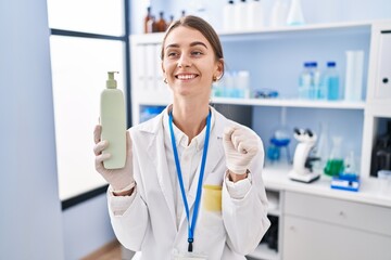 Canvas Print - Young caucasian woman working at scientist laboratory holding body lotion screaming proud, celebrating victory and success very excited with raised arms