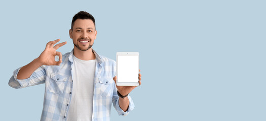 Handsome man holding tablet computer and showing OK on light blue background with space for text