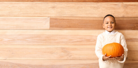 Sticker - Cute African-American boy holding pumpkin on wooden background with space for text