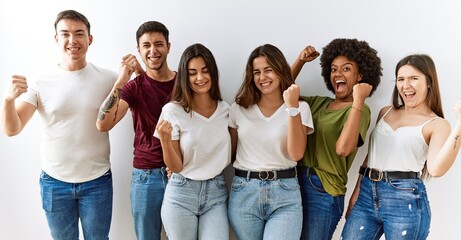 Poster - Group of young friends standing together over isolated background very happy and excited doing winner gesture with arms raised, smiling and screaming for success. celebration concept.