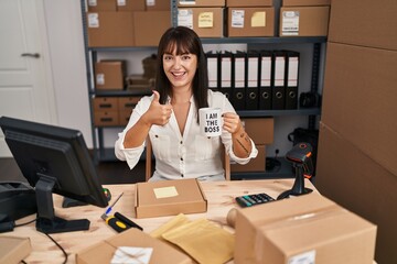 Sticker - Young brunette woman standing by manikin at small business holding i am the boss cup smiling happy and positive, thumb up doing excellent and approval sign