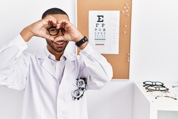 Poster - African american optician man standing by eyesight test doing heart shape with hand and fingers smiling looking through sign