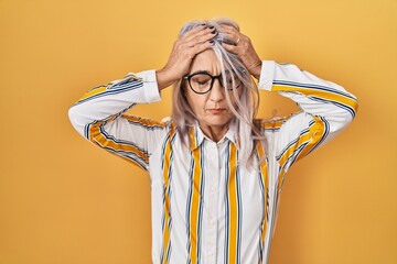 Sticker - Middle age woman with grey hair standing over yellow background wearing glasses suffering from headache desperate and stressed because pain and migraine. hands on head.