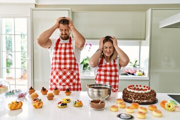 Wall Mural - Young couple cooking pastries at the kitchen suffering from headache desperate and stressed because pain and migraine. hands on head.