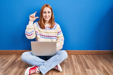 Canvas Print - Young woman using laptop at home sitting on the floor smiling and confident gesturing with hand doing small size sign with fingers looking and the camera. measure concept.