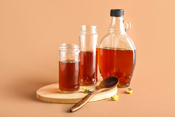 wooden board with jars and bottle of tasty maple syrup on color background
