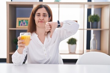 Sticker - Brunette woman drinking glass of orange juice looking unhappy and angry showing rejection and negative with thumbs down gesture. bad expression.