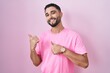 © Krakenimages.com - Hispanic young man standing over pink background pointing to the back behind with hand and thumbs up, smiling confident
