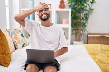 Poster - Hispanic young man using computer laptop sitting on the bed stressed and frustrated with hand on head, surprised and angry face