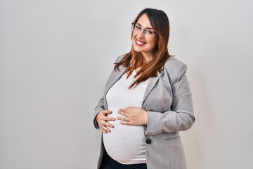 Poster - Pregnant business woman standing over white background with serious expression on face. simple and natural looking at the camera.