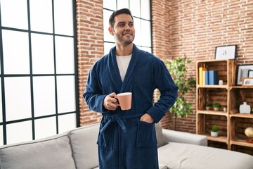 Wall Mural - Young hispanic man wearing robe drinking coffee at home