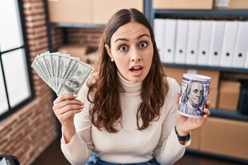 Sticker - Young hispanic woman working at small business ecommerce holding money and piggy bank in shock face, looking skeptical and sarcastic, surprised with open mouth