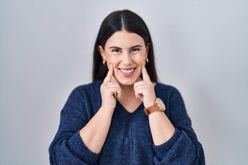 Poster - Young brunette woman standing over isolated background smiling with open mouth, fingers pointing and forcing cheerful smile