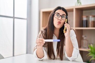 Sticker - Young brunette woman holding pregnancy test result speaking on the phone looking at the camera blowing a kiss being lovely and sexy. love expression.