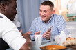 © JackF - Two positive male friends using mobile and talking in home interior