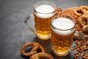 Wall Mural - Mugs of fresh beer and pretzels on dark background, closeup. Oktoberfest celebration