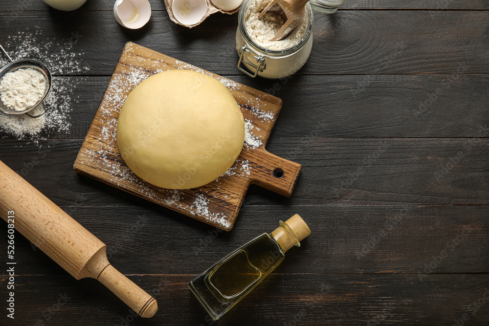 Raw dough with ingredients and utensils on dark wooden background