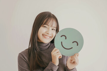 Wall Mural - Happy young Asian woman holding smile emoji face, positive mental health concept