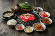 © daewoong - Bulgogi, a traditional Korean food on a black stone plate with a wooden background, and side dishes 나무배경에 검은 돌판위에 있는 한국 전통 음식인 불고기와 밑반찬