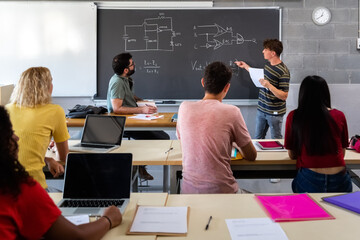 Teen male high school student giving oral class presentation in front of multiracial classmates. Teacher taking notes.