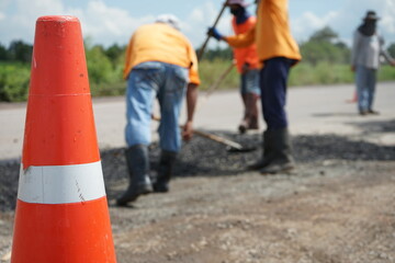 Blurred image of road maintenance work in Asia and there is an orange cone in front.