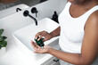© gpointstudio - High angle view of African-American woman standing in the bathroom and applying pills