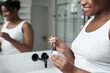 © gpointstudio - Side view of African-American woman using serum to face in the bathroom