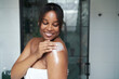© gpointstudio - African-American woman moisturizing the skin of arm in the bathroom