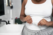 © gpointstudio - Close up of unrecognizable African-American woman standing in the bathroom and taking measures on her waist