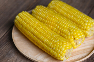 Wall Mural - cooked sweet corn on wooden plate background, ripe corn cobs steamed or boiled sweetcorn for food vegan dinner or snack