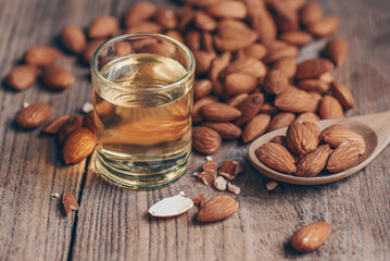 Poster - Almond oil and Almonds nuts on wooden, Delicious sweet almonds oil in glass, roasted almond nut for healthy food and snack organic vegetable oils for cooking or spa concept