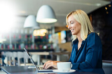 Smiling Freelancer Typing On Laptop Sitting At Cafe