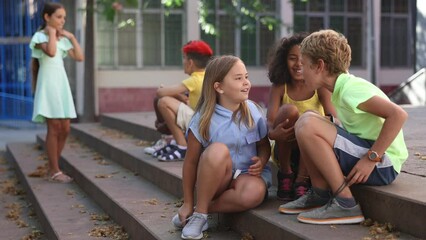 group of multiracial boys and girls sitting on stairs outdoors and having conversation.
