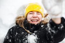 Close Up Portrait Of Funny Happy Teenage Girl In Yellow Knitted Hat Playing With Snow Outdoors