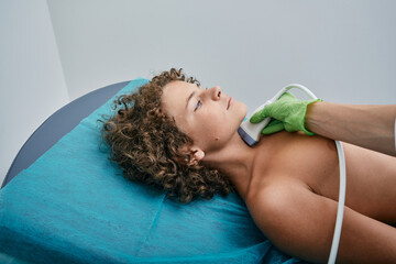 Boy patient receives thyroid gland diagnostics. Exam endocrine system of child at medical clinic with ultrasound machine