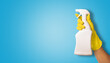 © ronstik - hand in yellow rubber glove holding white blank cleaning spray bottle on blue background. copy space