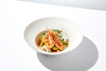 Canvas Print - Elegant food - salad with shrimp and avocado on white table with harsh shadow. Flashy food concept. Seafood salad with shrimp, tomatoes and avocado on white plate with sunlight