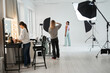 Photographer standing and shooting model while make up artist standing at her workplace