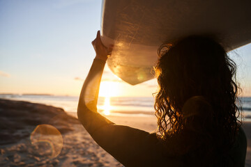 Beautiful woman carrying surfboard at her head while preparing for the surf