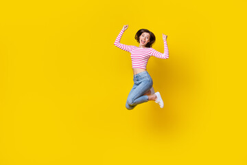 Full length photo of girlish adorable pretty woman dressed striped top jeans sneakers jumping hands up isolated on yellow color background